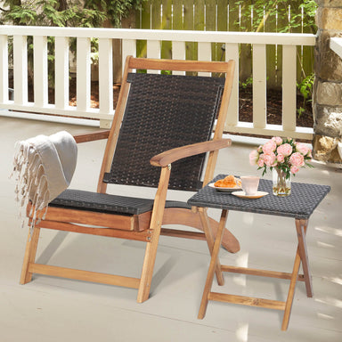 Stylish 2 Pieces Patio Rattan Folding Lounge Chair with Acacia Wood Table, featuring a cozy setup with a soft throw and a decorative flower arrangement on the table.