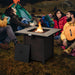 Enjoying a cozy evening around the 30-inch square propane gas fire pit table with ceramic tabletop from Dream Yard Oasis™, surrounded by friends at a campsite.