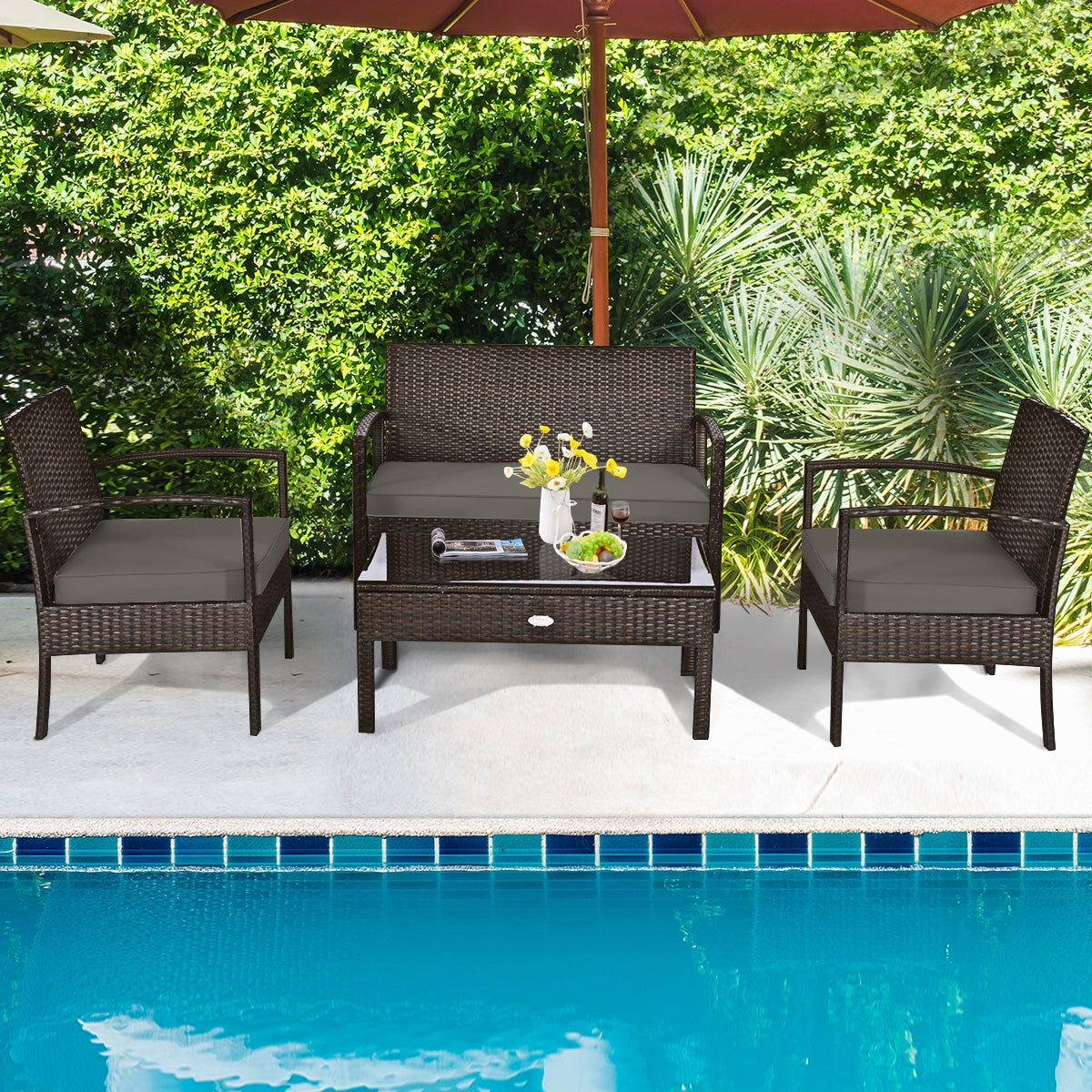 4-Piece Patio Rattan Furniture Set with Cushions, Loveseat, & Table - Brown Outdoor Bliss arranged by a pool, with decor items on the coffee table and vibrant greenery around.