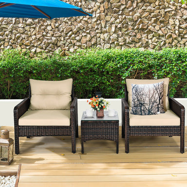 3-Piece Beige Rattan Outdoor Patio Conversation Set with Cushions & Tempered Glass Table set against a stone wall and greenery, perfect for outdoor relaxation.