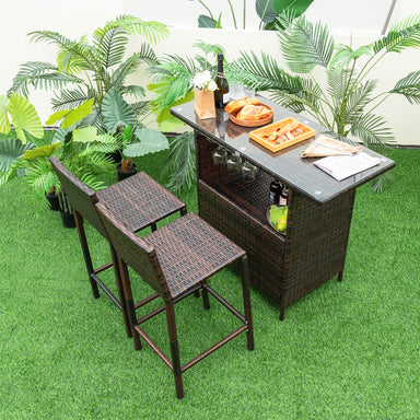 3-Piece Outdoor Wicker Bar Set with 3-Row Stemware Racks, Comfortable Seating & Durable Frame arranged in a lush green outdoor setting, featuring two bar chairs and a table with drinks and snacks.