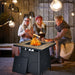 28" 40,000 BTU Propane Gas Fire Pit Table with Cover, Lava Stones & CSA Certification, showing a fun outdoor gathering with kids roasting marshmallows by the fire.