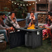 Group of friends enjoying the 32-Inch Propane Fire Pit Table with Lava Rocks, 50000 BTU, CSA Certified, Black, sharing warmth and laughter around the fire.