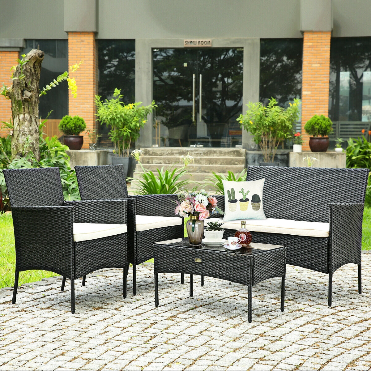 4-Pc Outdoor Patio Rattan Sofa Set with Cushions set in a lush garden, showcasing the black rattan chairs and table with decorative elements.