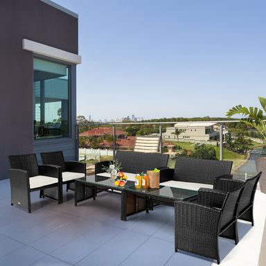 4-Piece Weather-Resistant Rattan Patio Seating Set with Cushions & Glass Coffee Table displayed on a modern balcony, featuring stylish black rattan chairs and a coffee table with a glass surface.