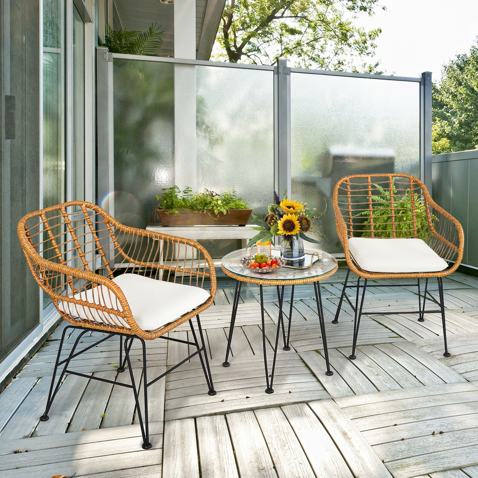 Stylish balcony view with the 3-Piece White Rattan Furniture Set with Cushioned Chairs and Glass Top Table for Outdoor Relaxation, highlighting two comfortable rattan chairs, a round table, and a decorative arrangement with sunflowers.