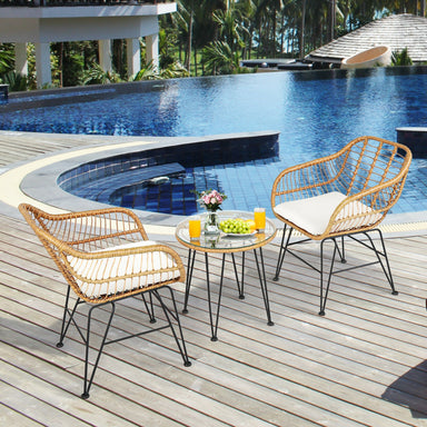 3-Piece White Rattan Furniture Set with Cushioned Chairs and Glass Top Table for Outdoor Relaxation, placed by a poolside, featuring two elegant rattan chairs and a stylish glass-top coffee table with drinks and decor.