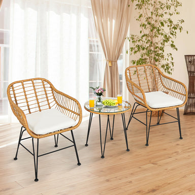 Cozy indoor setting showcasing the 3-Piece White Rattan Furniture Set with Cushioned Chairs and Glass Top Table for Outdoor Relaxation, featuring two rattan chairs and a glass table, surrounded by sunny curtains.