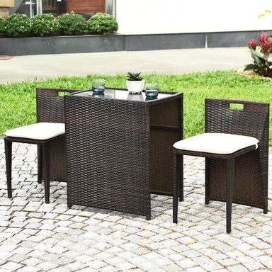 3-Piece Outdoor Wicker Patio Set with Cushions, No Assembly, Space-Saving Glass Table displayed on cobblestone with a green garden background, including two comfortable chairs and a modern table.