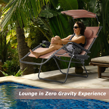 Folding Recliner Lounge Chair With Adjustable Shade Canopy & Cup Holder - Coffee, providing a zero-gravity experience. A woman lounges by a pool surrounded by tropical plants, showcasing comfort and style.