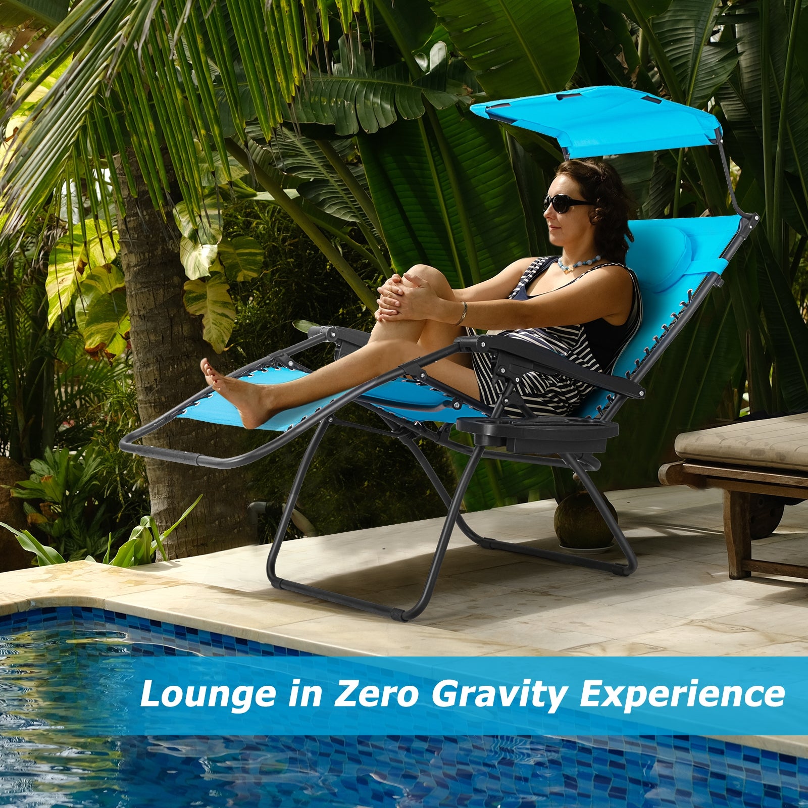 Folding Recliner Lounge Chair With Adjustable Shade Canopy & Cup Holder - Durable Steel Frame - Blue. A woman lounging on a blue recliner chair by a pool surrounded by lush greenery.