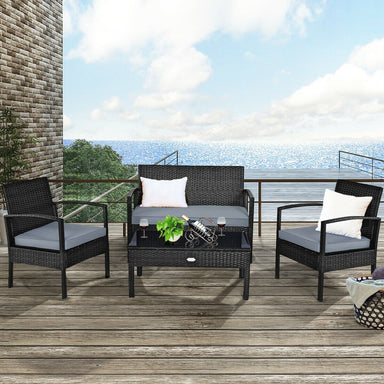 4-Piece Black Patio Rattan Furniture Set with Loveseat, Coffee Table & Cushions placed on a stylish outdoor deck with a view of the ocean, featuring soft gray cushions and decorative pillows.