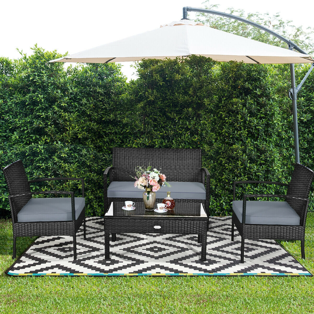 4-Piece Black Patio Rattan Furniture Set with Loveseat, Coffee Table & Cushions in a garden setting under an umbrella featuring a cozy arrangement with floral decor.